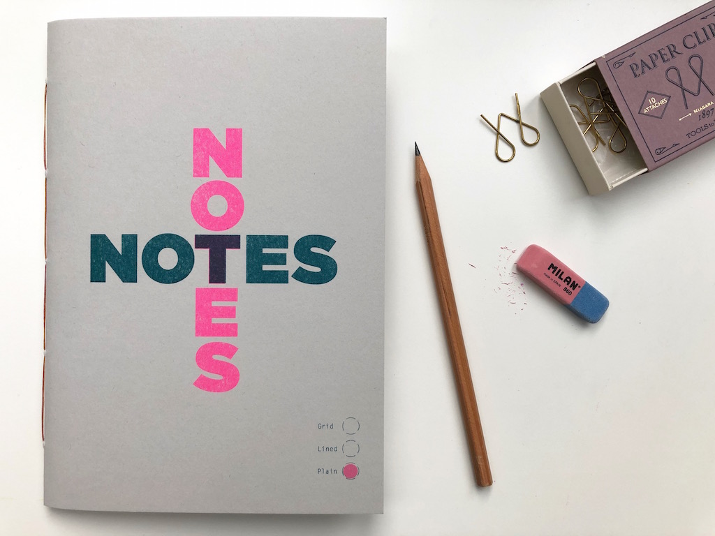A notebook, with desktop scene including a pencil, eraser and paperclips. 
