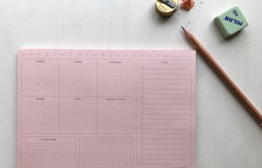 A pink planner pad with a pencil, sharpener and eraser