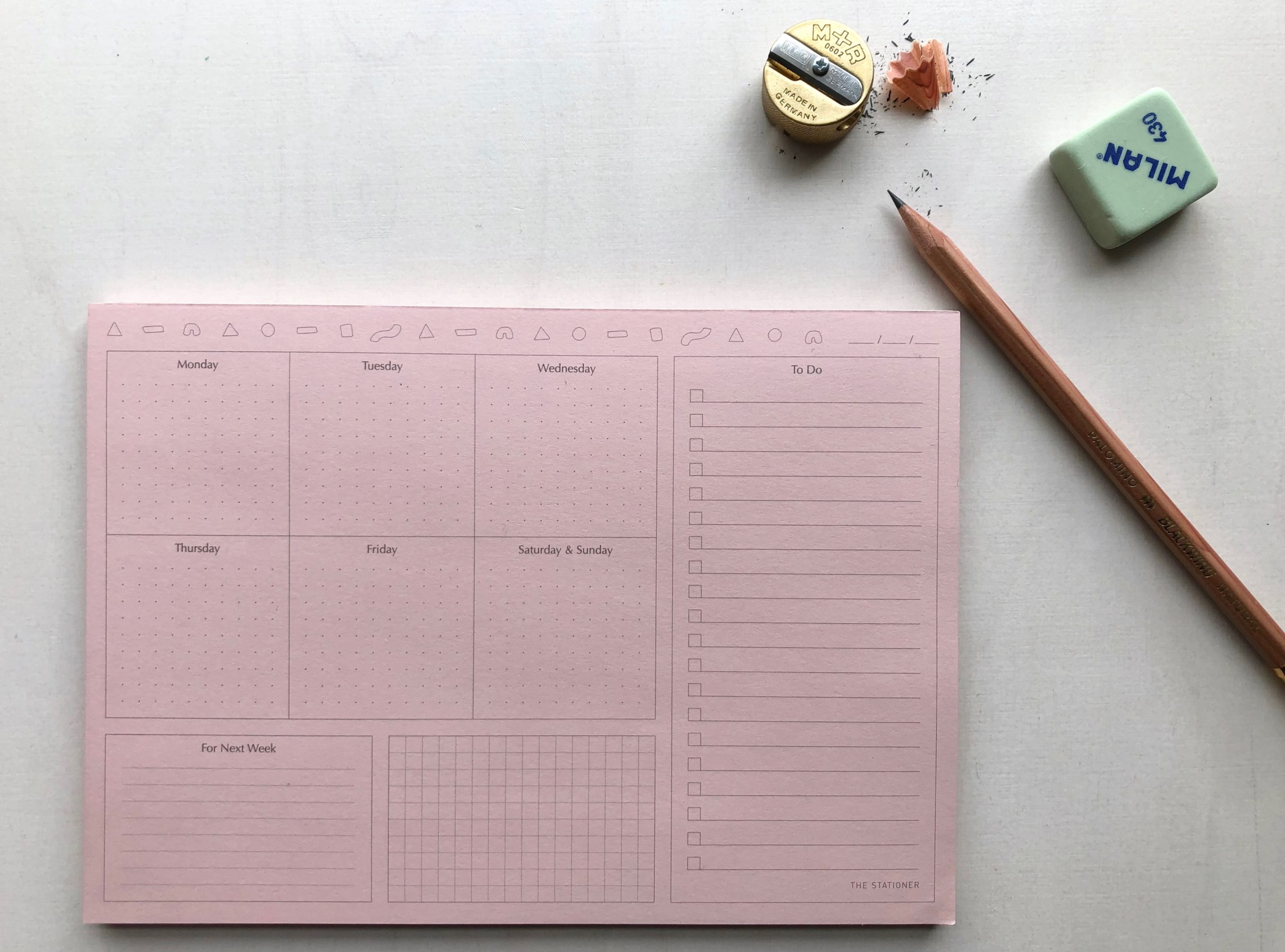 A pink planner pad with a pencil, sharpener and eraser